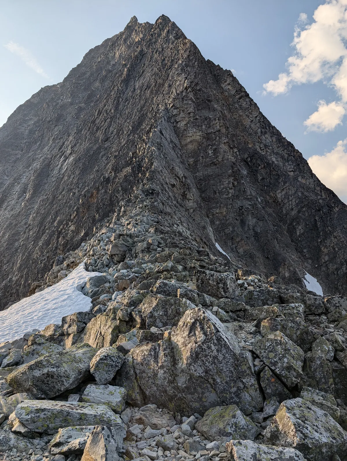 The dark face of Sir Donald rising above a boulder field and a patch of snow.